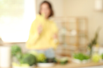 Beautiful young woman with different fresh green vegetables in kitchen, blurred view