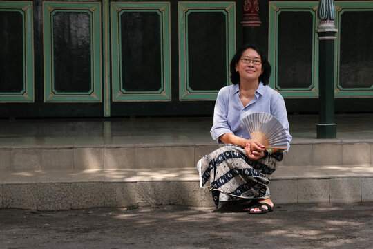 Javanese woman sitting alone on the floor in front of old Javanese architectural house