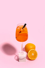 Glass of Aperol spritz cocktail and oranges on pink background