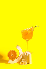 Decorative podiums with glass of Aperol spritz cocktail and half of orange on yellow background