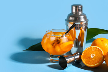 Glass of Aperol spritz cocktail with oranges and shaker on blue background