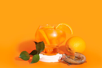 Decorative podium with glass of Aperol spritz cocktail on orange background