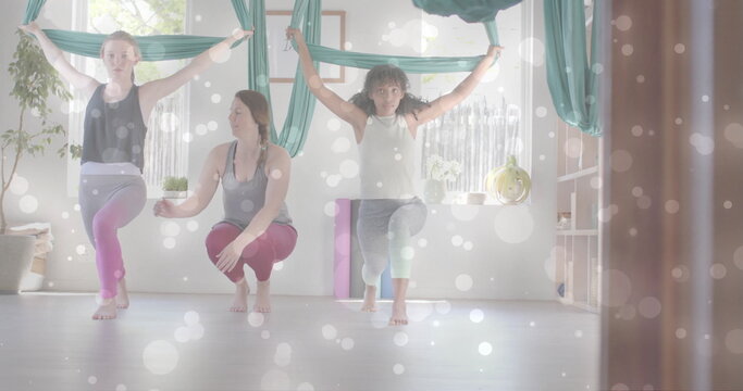 Image of white light spots over diverse female instructor and teenage girls doing aerial yoga - Powered by Adobe