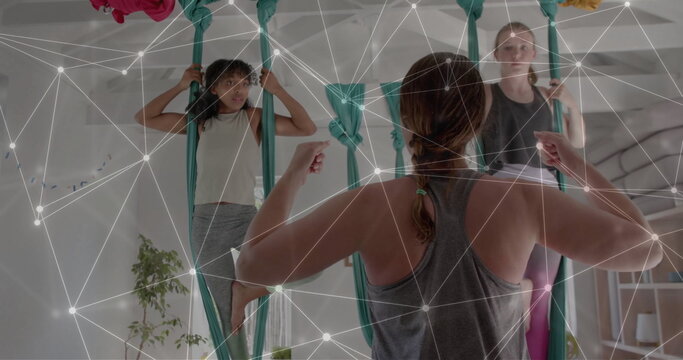 Image of network over diverse female instructor and teenager girls practicing aerial yoga