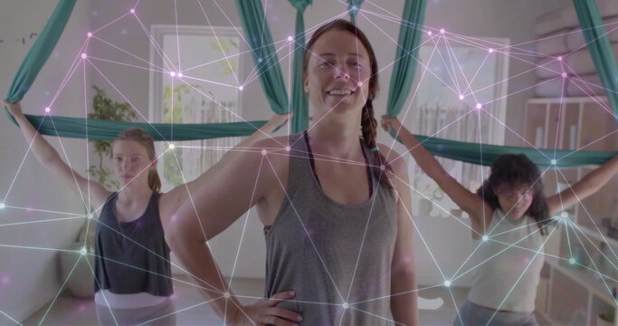 Image of glowing network over diverse female instructor and teenage girls practicing aerial yoga - Powered by Adobe