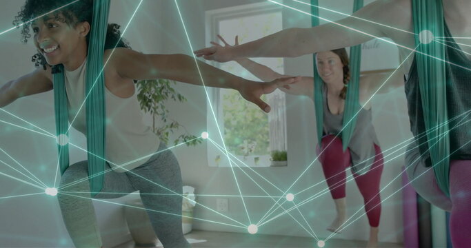 Image of glowing network over diverse female instructor and teenage girls practicing aerial yoga - Powered by Adobe