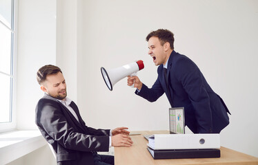 An angry boss with a megaphone yells at an employee in the office, close-up. Concept of shouting in...