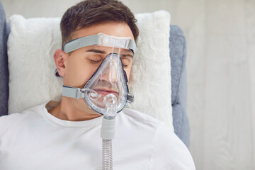 Closeup from above sick man with a medical oxygen mask on face lying on a soft pillow on the couch...