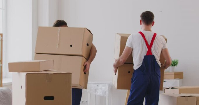 Moving delivery service, male movers moving cardboard boxes, loading, unloading and setting up of household goods, new house stuff, carrying stacks of cardboard relocation boxes in office room