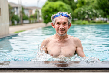 portrait happy elderly man with goggles in swimming pool,healthy asian senior male enjoying his...