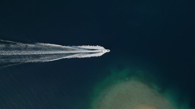 Aerial view of a lone boat speeding across the calm, dark blue ocean, leaving a trail of white waves behind. The simplicity and tranquility of the vast sea contrast with the boat's motion