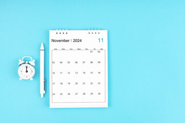November 2024, Monthly desk calendar for 2024 year and pen with alarm clock on blue background.