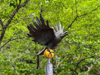 Crow statue standing on golden ball in woods