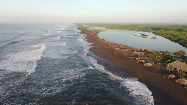 Aerial view of sandy beach with tranquil waves and huts, El Paredon, Guatemala.