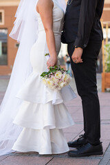 The bride stands opposite the groom. Photo of the bride and groom without faces. The bride holds a...