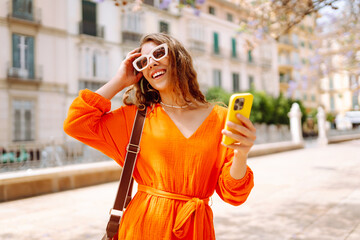 Fototapeta premium Happy young travel woman using mobile phone and relax on street market. Travel, tourism, technology, blogging, communication concept.