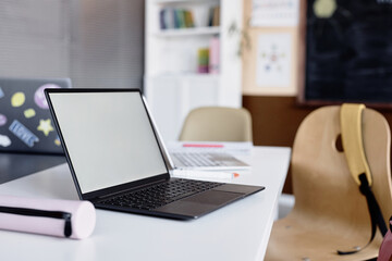 Side view of blank mockup screen of open laptop on desk in empty classroom, copy space