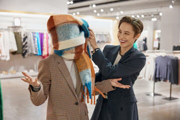 Joyful female friends fooling around while shopping at clothes store