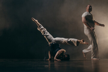 Couple of fighters training capoeira on black background