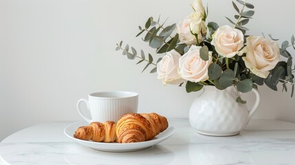 On a white marble table there is a vase with white roses, aromatic coffee in a cup, crispy fresh croissants