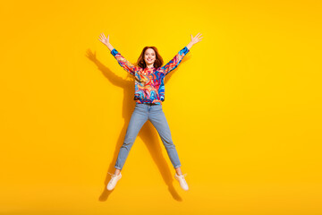 Full size photo of optimistic adorable cute girl dressed print shirt jeans flying raising hands up isolated on yellow color background