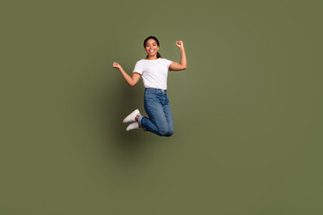 Full length photo of american girl wear white t shirt and jeans jumping overjoyed celebrate party isolated on khaki color background