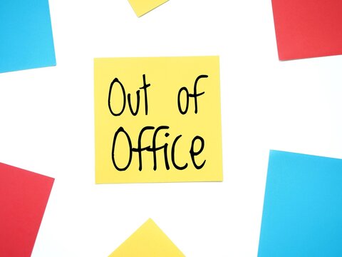 A yellow sticky note with the handwritten text Out of office in black letters. Is it correct: out-of-office message on a paper note