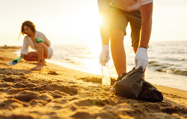 Cleanup garbage on the ocean coast. Volunteers with polyethielene bag picking up a plastic bottle...