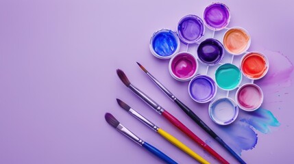 Naklejka premium Watercolor paints and brushes on a lilac backdrop Aerial view Art and learning idea
