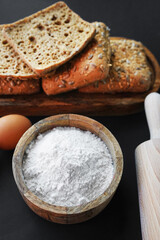 Small fresh breads with seeds and sesame on a wooden tray next to eggs, a wooden bowl with flour and a rolling pin