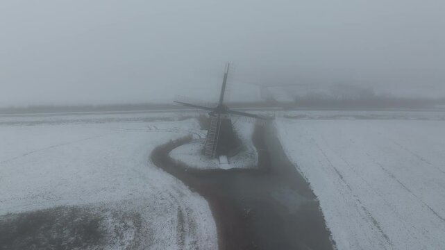 Aerial view of snow-covered landscape with windmill and fog, Holwerd, Friesland, Netherlands.