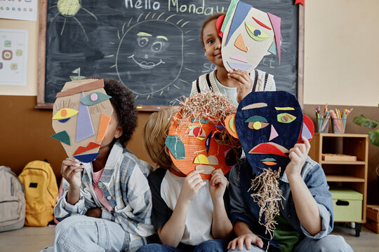 Group of four kids in classroom holding handmade cardboard abstract faces presenting art project results
