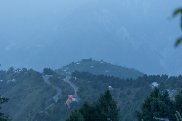 Scenic winding road meanders through verdant mountains on a misty day, offering a tranquil and...