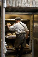 A baker pushes a cart with bread into an oven