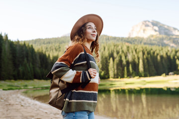 Active woman with backpack solo travel near lake on wooded mountains background. Adventure and travel exploring. Hiking.