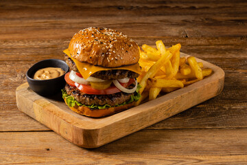 Classic beef burger. Served in a set with fries. Wooden, natural background. Dark styling.