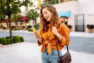 Young woman using a smart phone while walking on a sidewalk in the city. Business, technology, blogging, communication concept.