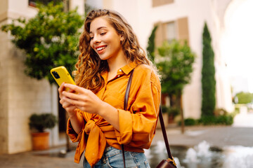 Young woman using a smart phone while walking on a sidewalk in the city. Business, technology,...
