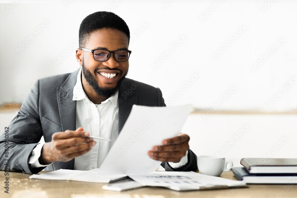 Poster a man in a suit is sitting at a desk, reviewing documents. he is smiling and holding a pen in his ha