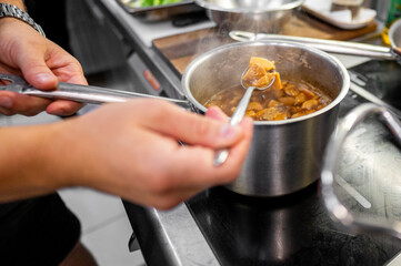 Close-up of hands stirring stew in a pot, emphasizing steam and texture