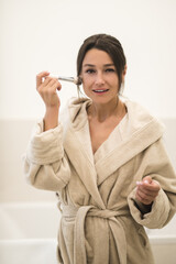 Slim cute young woman in a home robe doing make up