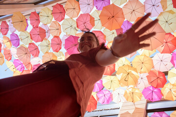 A joyful young woman reaching towards the camera below a vibrant ceiling of multicolored umbrellas.