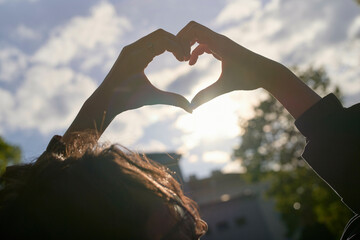 Silhouetted hands form a heart shape against a soft sunset sky.