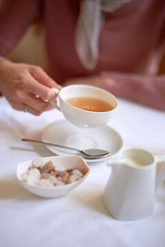 Elegant tea time with a person enjoying a cup of tea, complete with milk and sugar on the side.