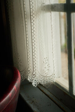 White lace curtain with an intricate design hangs by a vintage wooden window with soft light filtering through.