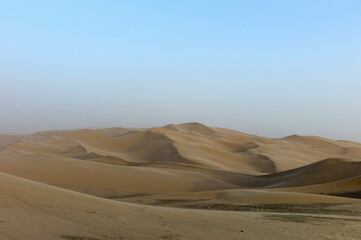 Smooth sand dunes under a hazy sky in a vast desert landscape.