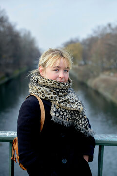 Woman in a leopard print scarf leaning on a bridge railing with a river and trees in the background on a foggy day.