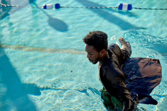 Man swimming in a pool with clothes on during a sunny day.
