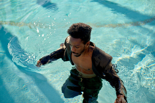 A man in a suit wades through clear blue water, looking focused and determined.