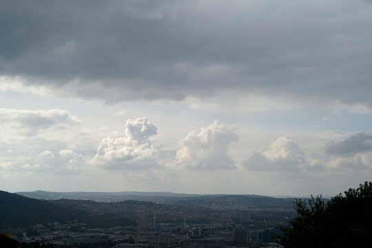 Overcast sky above a sprawling cityscape with visible cumulus clouds and an expansive view of urban buildings set against a hilly backdrop.